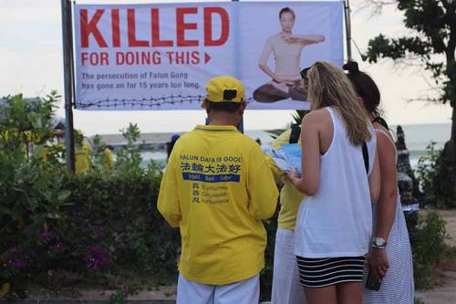 图3-4:在游行队伍中沙滩行走时,有的学员向身边的游客们讲真相,发资料,帮助中国游客退出党团队。游客们专心的倾听法轮功学员讲真相。