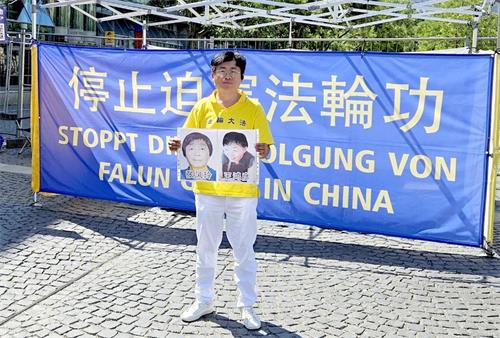 '图2：我在2025年7月19日德国法兰克福的“7·20”纪念活动上举着我熟悉的、2025年初相隔一个月去世的母女法轮功学员遗像，纪念那些在迫害中失去生命的法轮功学员。'